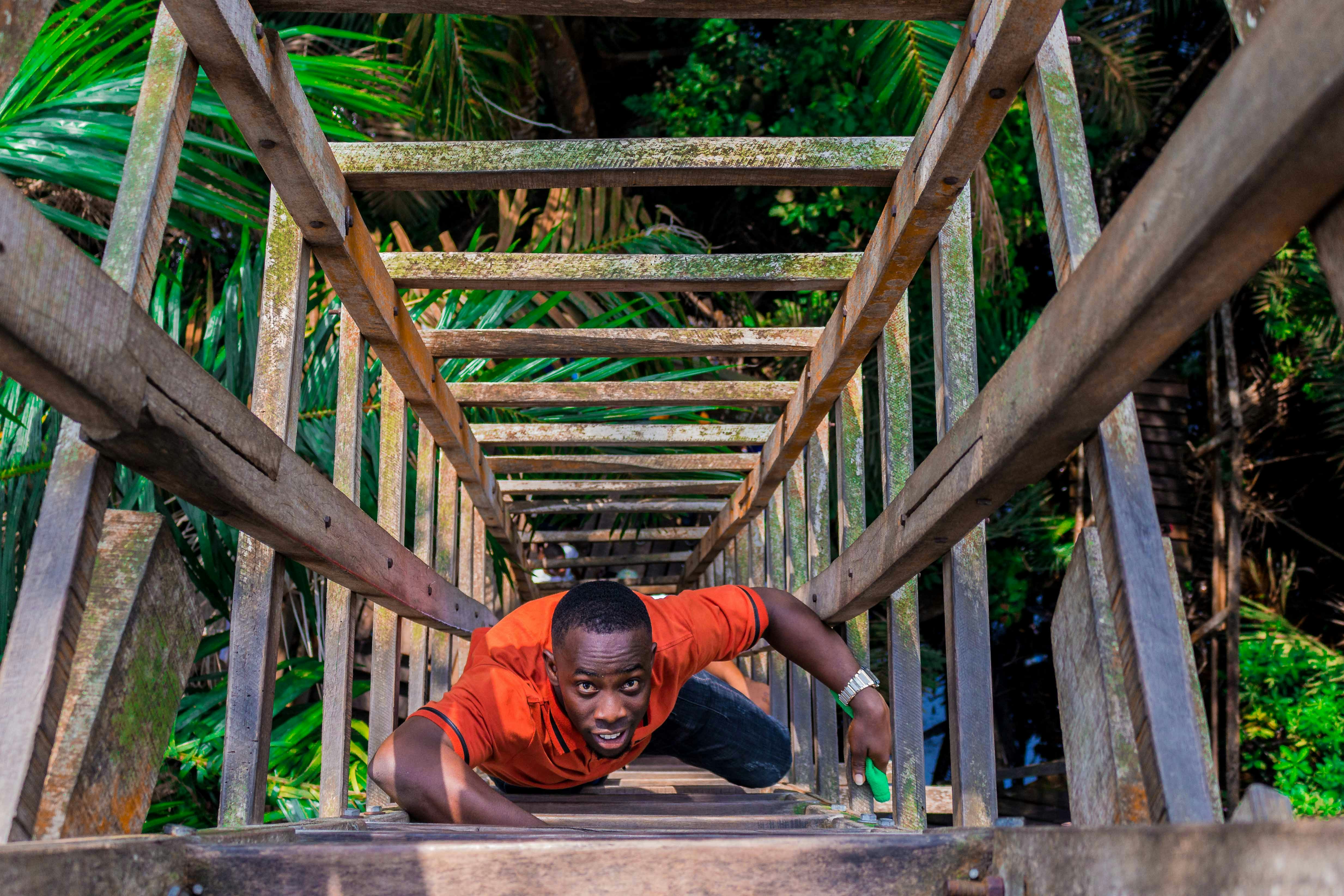 Femme en chemise à manches longues orange et pantalon noir assise sur un pont en bois marron