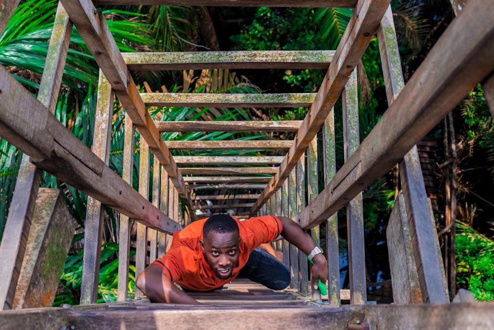 woman in orange long sleeve shirt and black pants sitting on brown wooden bridge