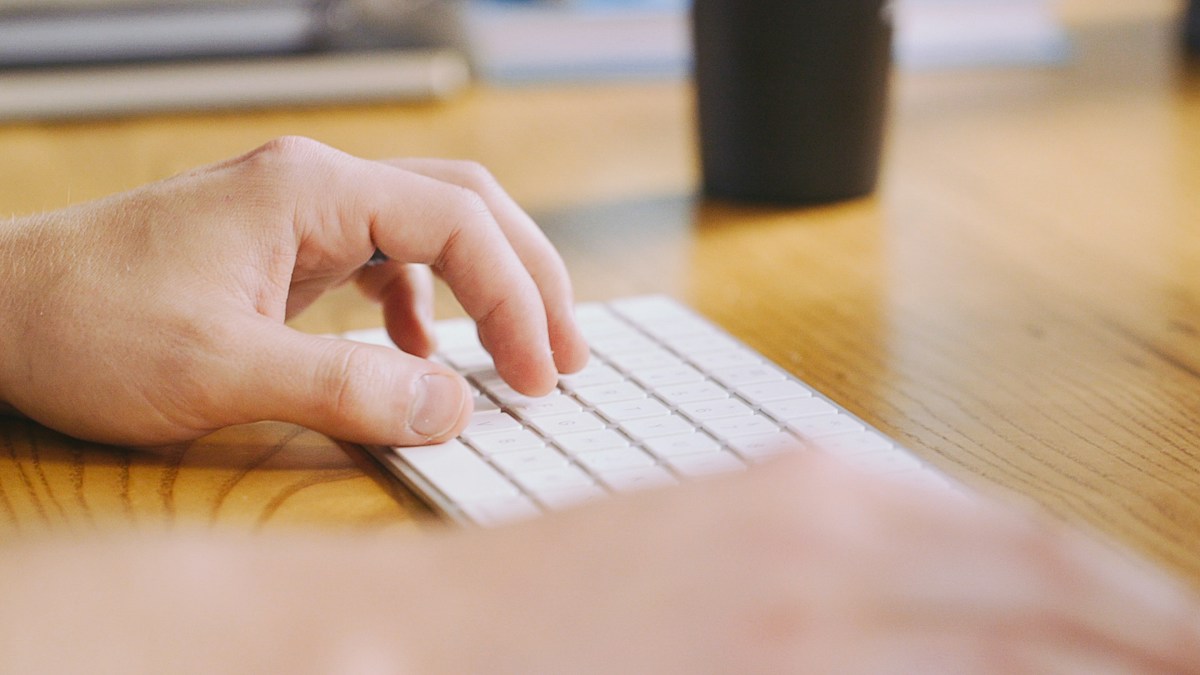 A person's hand typing on a white keyboard, planning low-cost volunteer appreciation gifts and ideas.