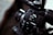 Close-up of a Canon video camera focusing on the control panel with buttons and switches, showing the brand logo prominently. The imaging device has a sleek black finish, and the lens is partially visible.