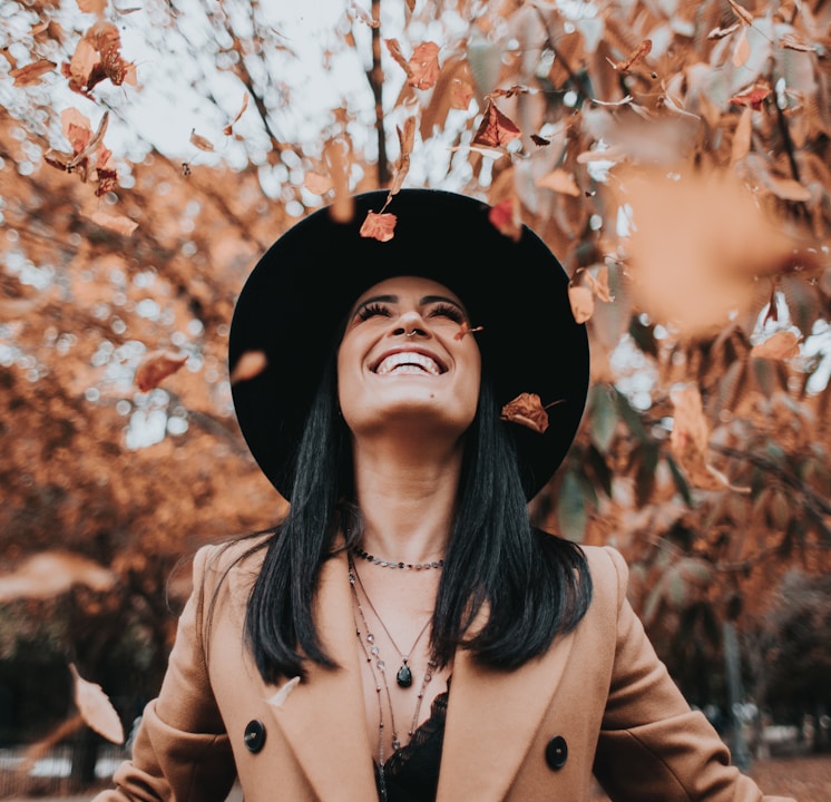 woman in brown coat and black hat standing under brown leaves tree during daytime