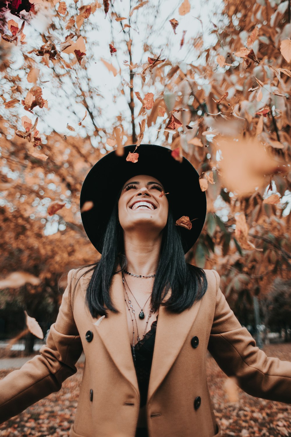 woman in brown coat and black hat standing under brown leaves tree during daytime
