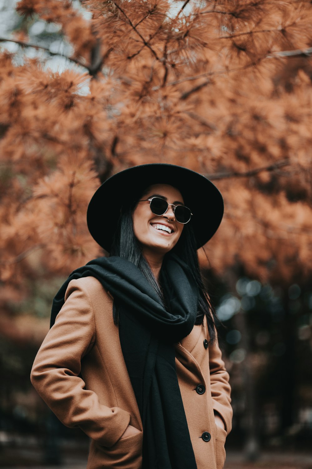 woman in black hat and brown coat standing near brown leaves tree during daytime