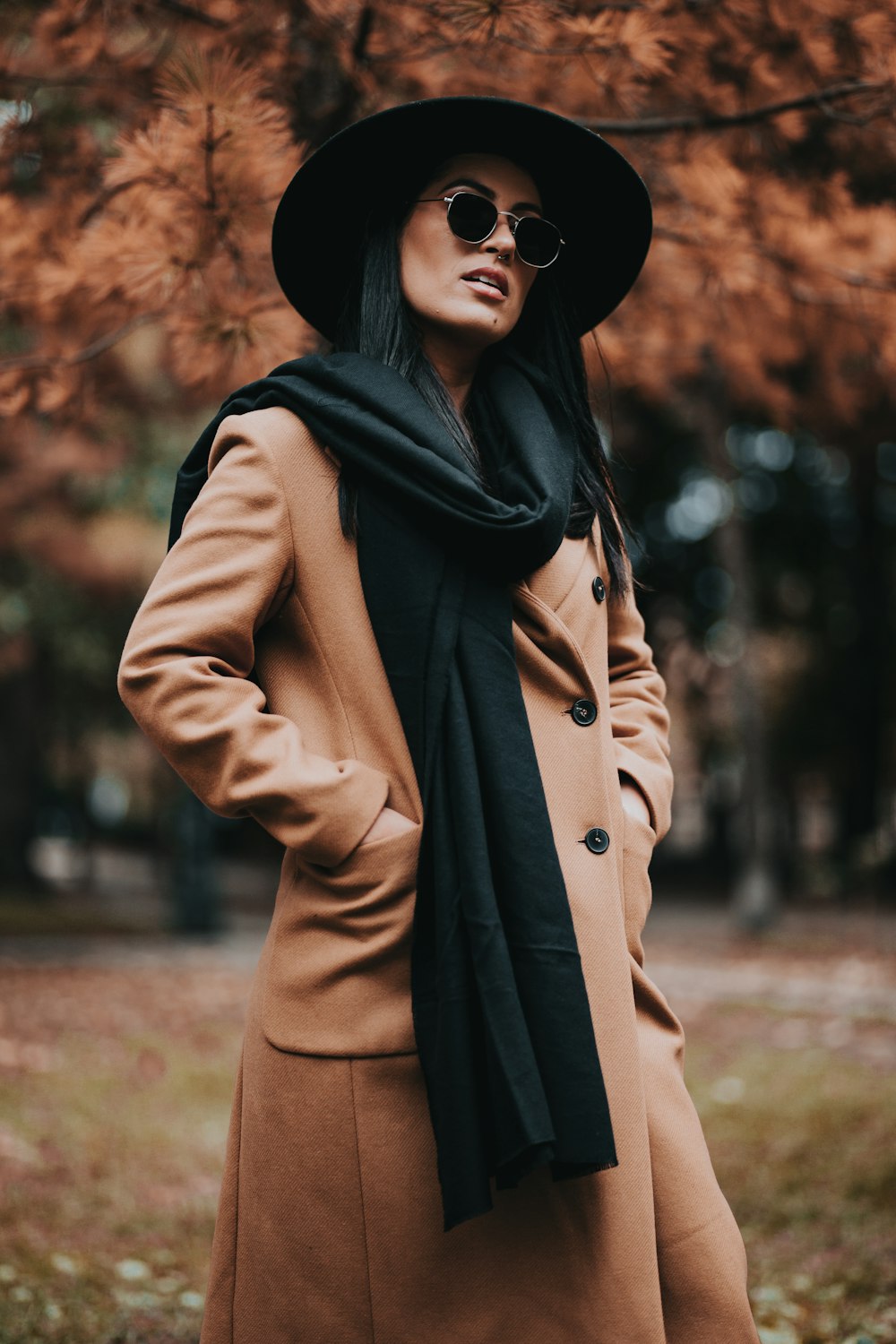 woman in brown coat and black hat standing near brown trees during daytime