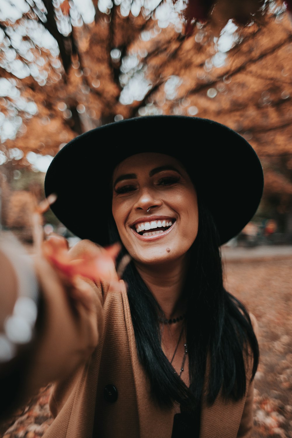 mulher sorridente vestindo chapéu preto e lenço marrom