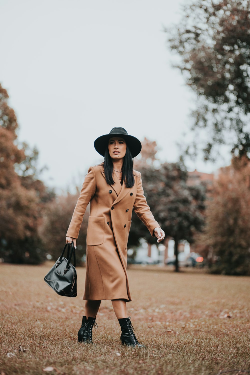 woman in brown coat holding black leather handbag