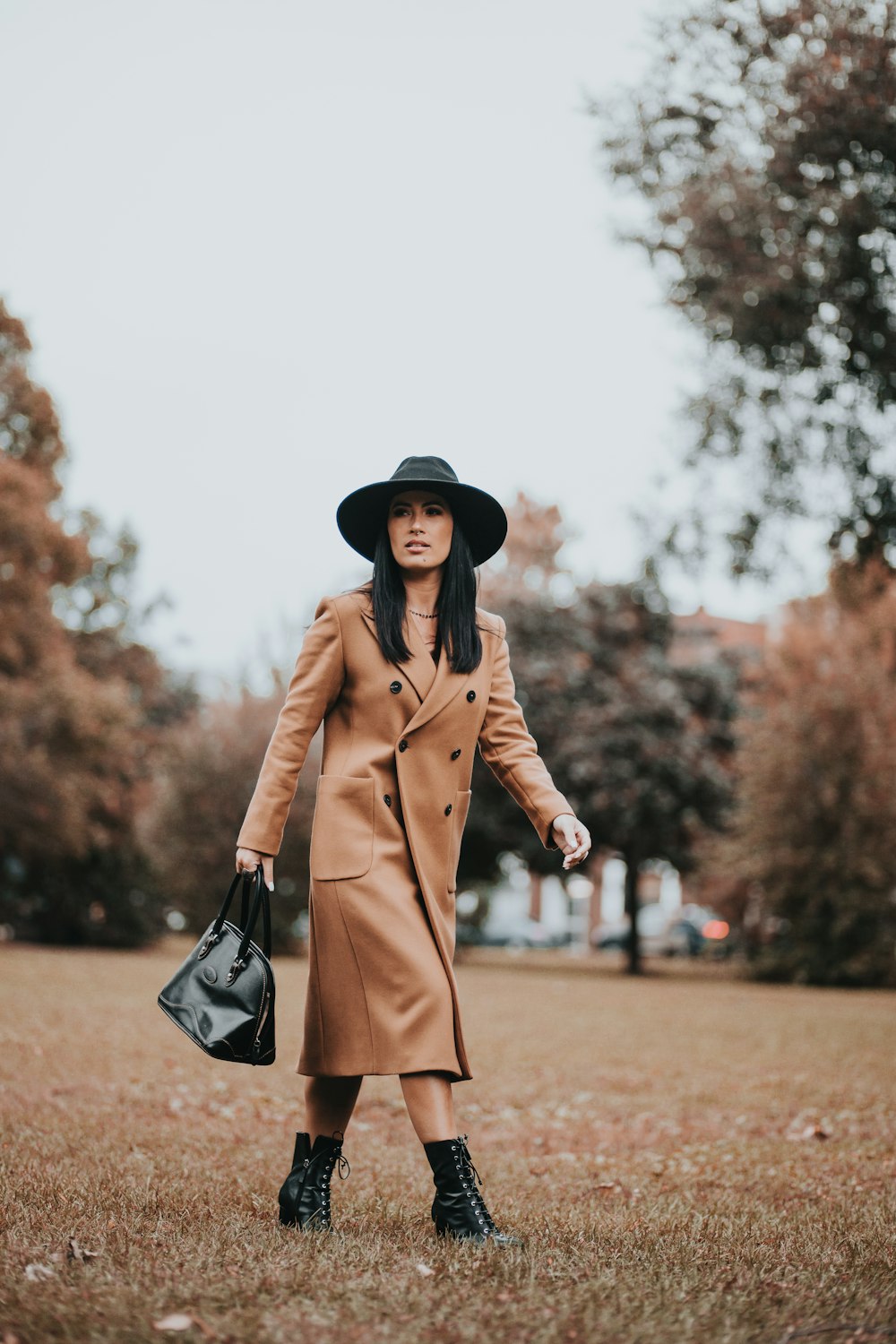 Femme en manteau marron tenant un sac à main en cuir noir