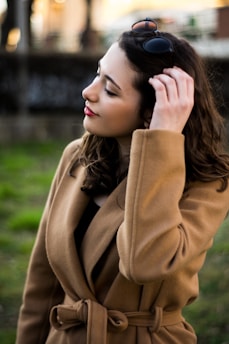 woman in brown coat standing near green grass during daytime