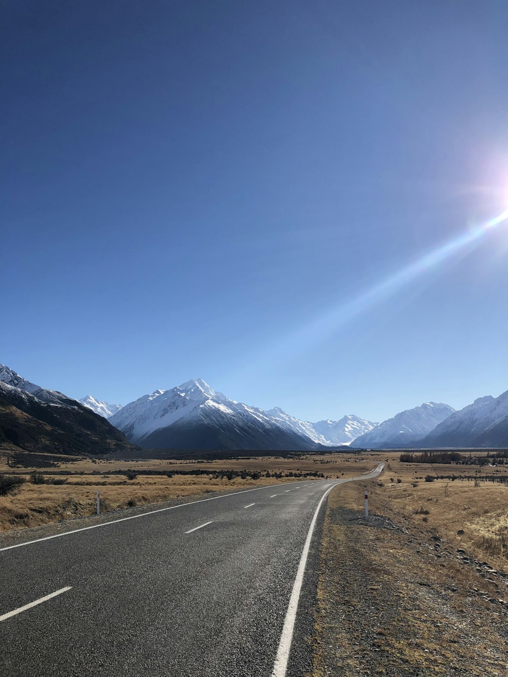 昼間の青空の下、山の近くの灰色のコンクリート道路