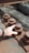 A close-up of a hand touching a large, rusted metal nut and bolt on an industrial structure. The bolts are lined up along a metal beam with a wooden surface beneath them.