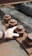 A close-up of a hand touching a large, rusted metal nut and bolt on an industrial structure. The bolts are lined up along a metal beam with a wooden surface beneath them.