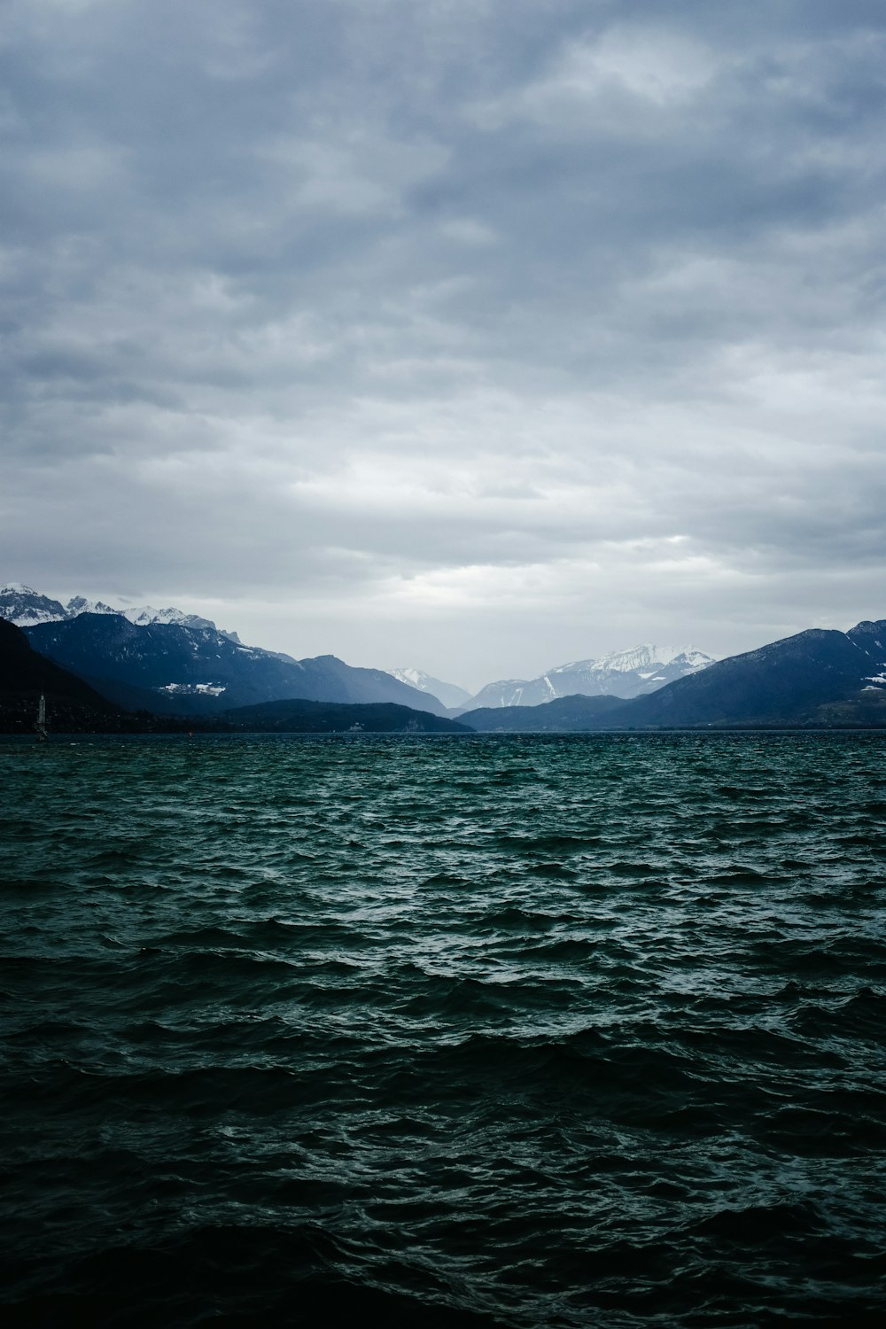 body of water near mountains under cloudy sky during daytime