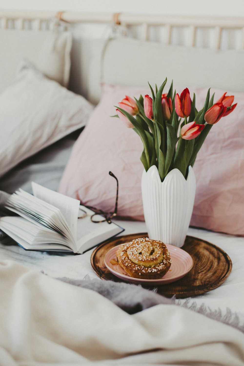 red tulips in white ceramic vase on brown wooden round tray