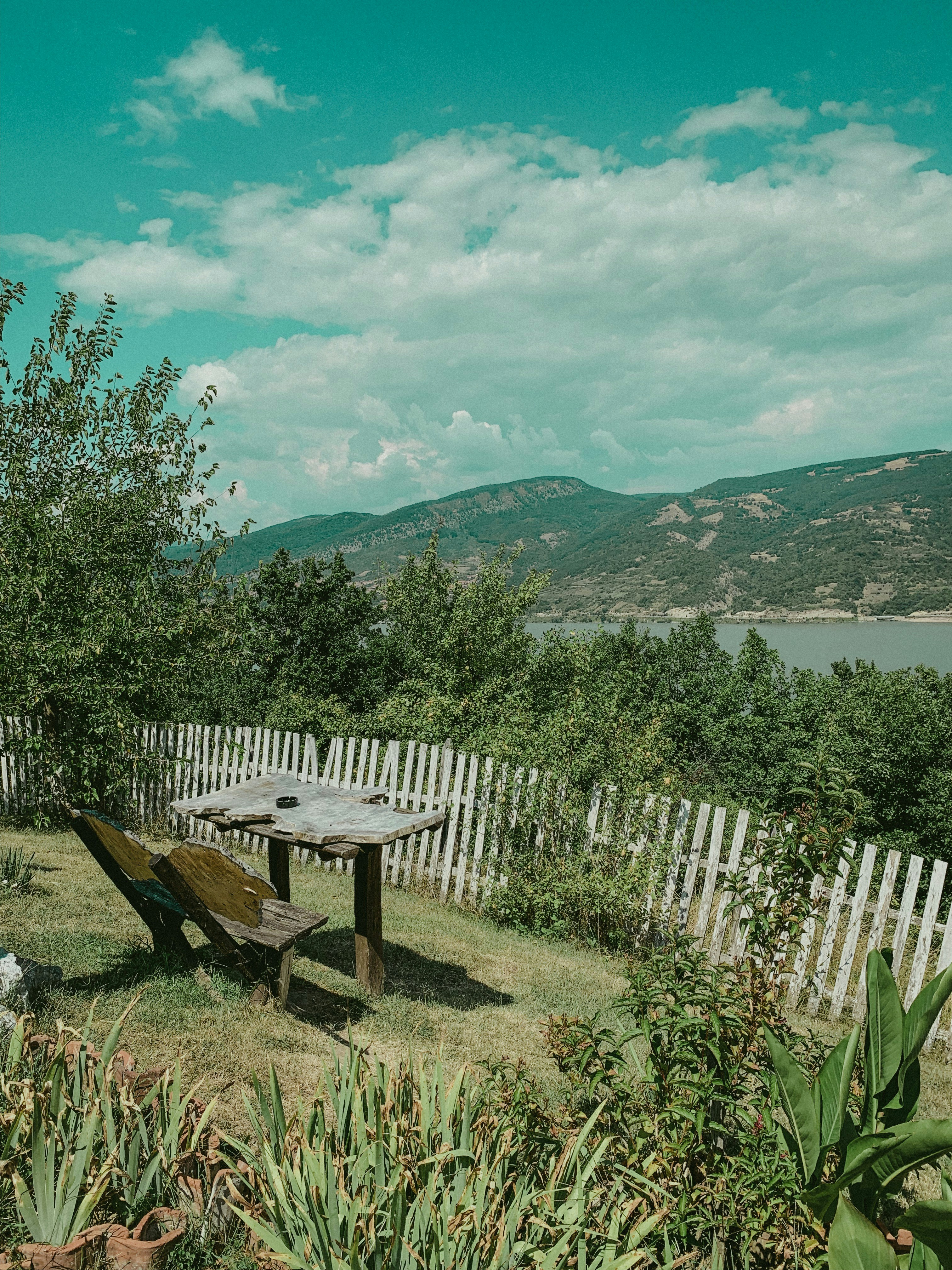 Brown wooden picnic table near white wooden fence and green grass field ...