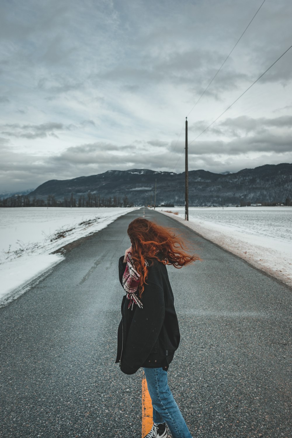 Femme en veste noire debout sur une route en béton gris pendant la journée