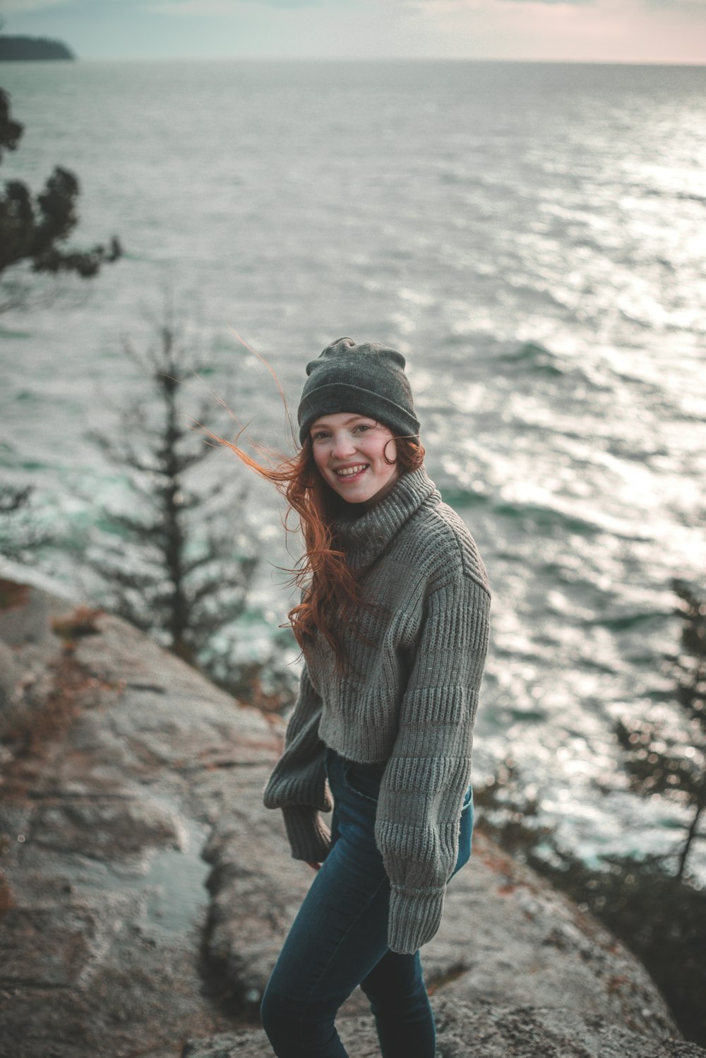 woman in gray knit sweater standing on rock near river during daytime
