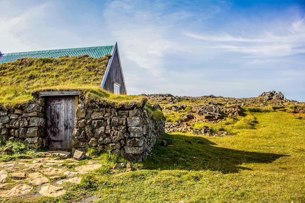 maison en bois marron sur un champ d’herbe verte sous des nuages blancs pendant la journée