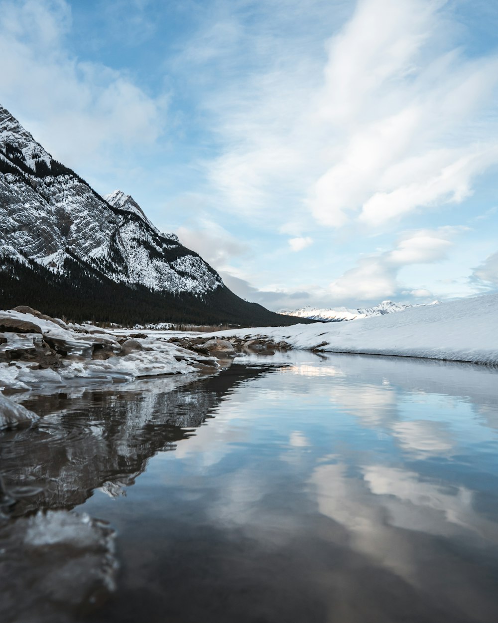 body of water near mountain under white clouds during daytime