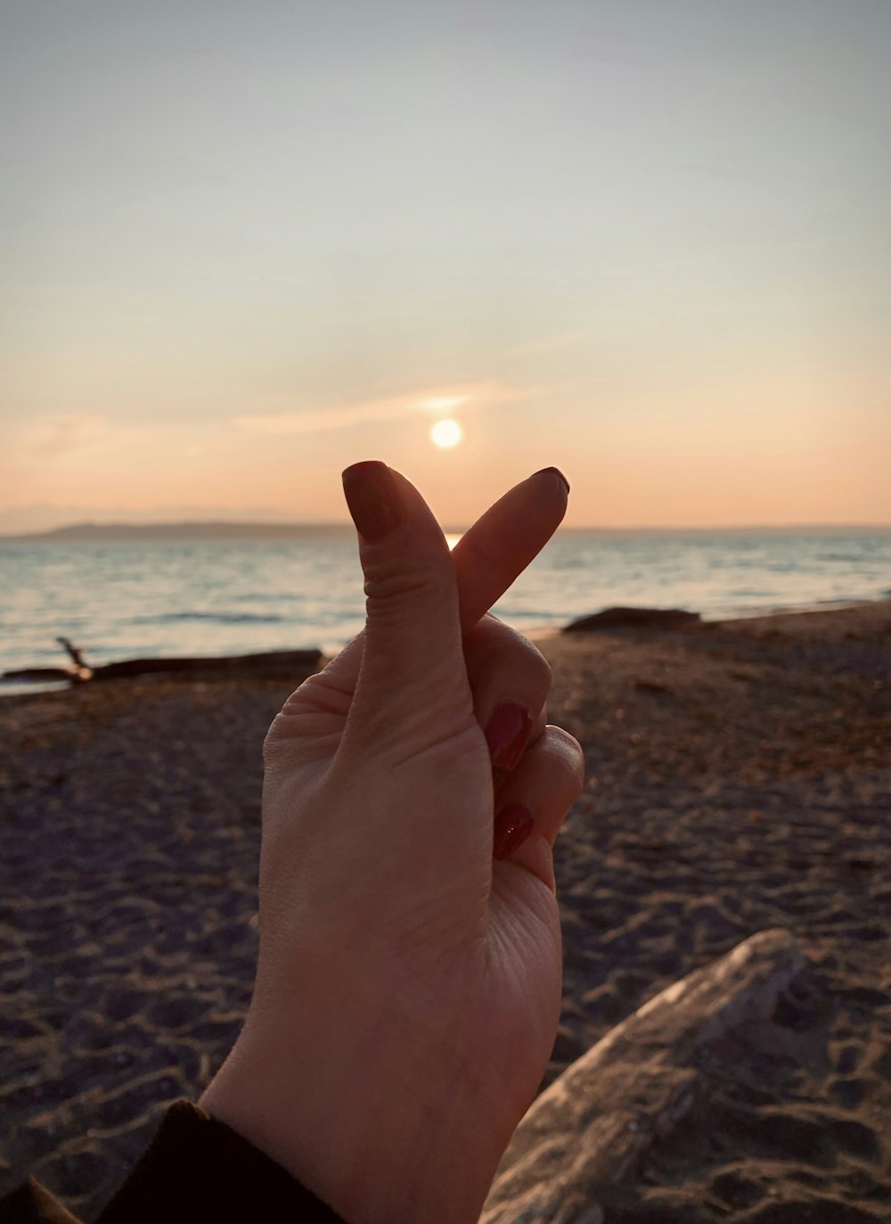 person showing right hand near body of water during sunset