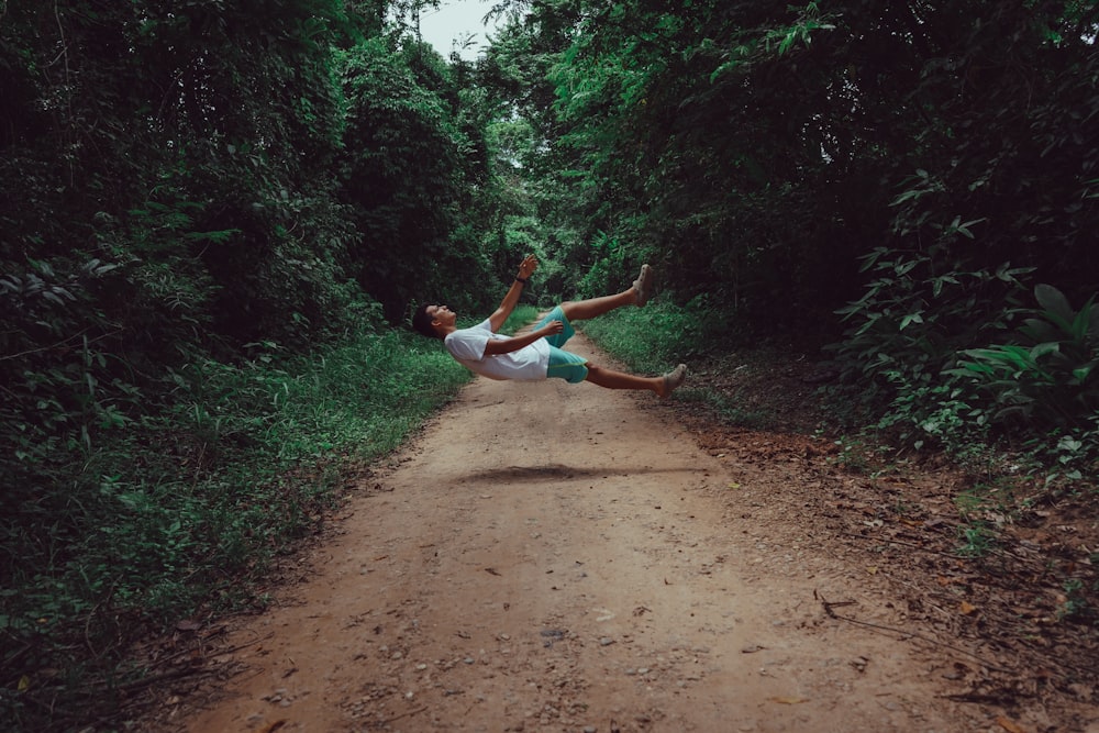 woman in white tank top and white shorts jumping on brown dirt road during daytime