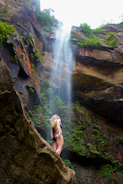 woman in black bikini sitting on rock near waterfalls during daytime