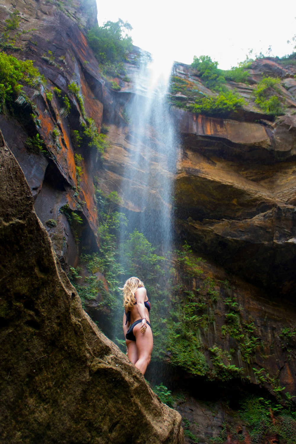 woman in black bikini sitting on rock near waterfalls during daytime