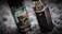 A vape device stands upright next to a bottle of vaping flavor liquid. The bottle features a label with bold text and an image of a gas mask. The vape device has a metallic finish with a clear tank on top.