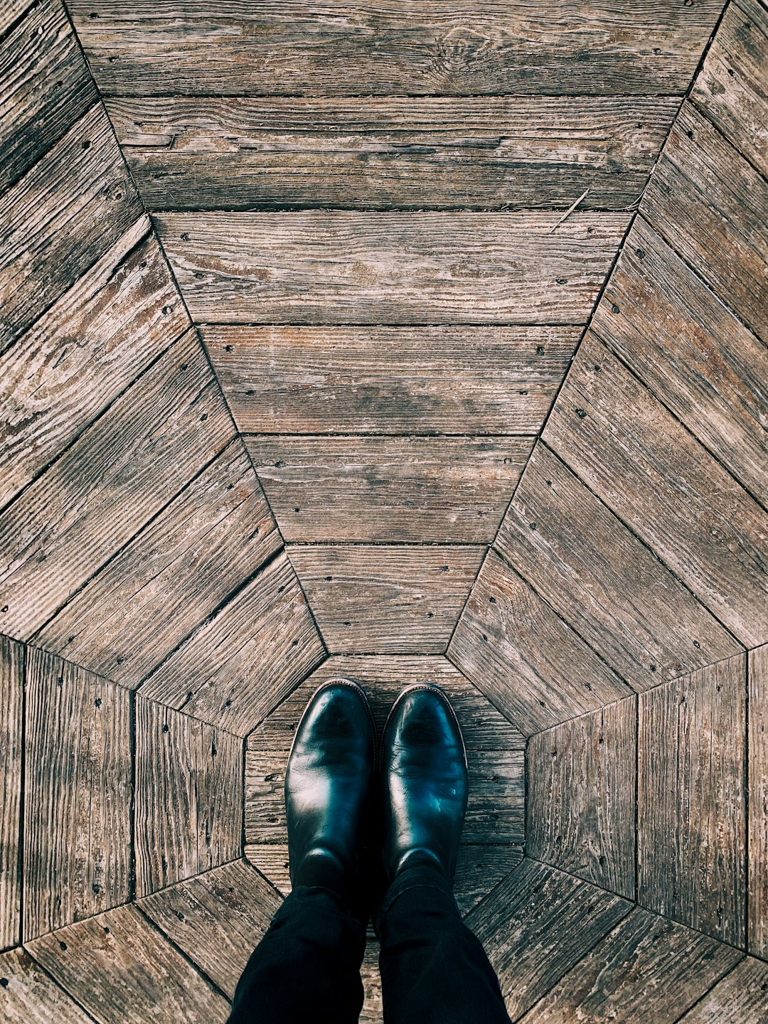 person wearing black leather shoes standing on wooden floor