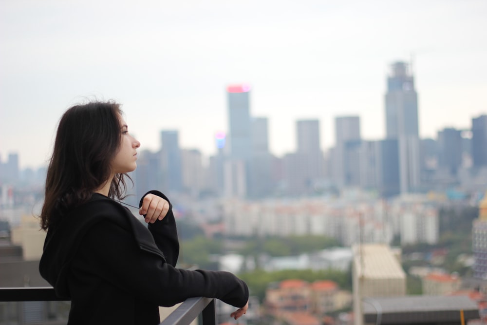 mulher na camisa preta de manga comprida olhando para a cidade durante o dia