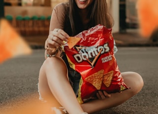 woman in black shirt sitting on the street holding red plastic pack