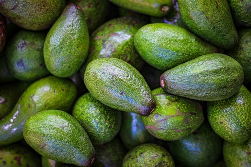 A close-up of ripe Hass avocados on a wooden table, showcasing their rich green color and texture.