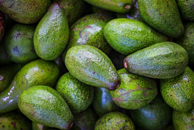 Close-up of ripe Haas avocados with deep green skin resting on a rustic wooden crate.