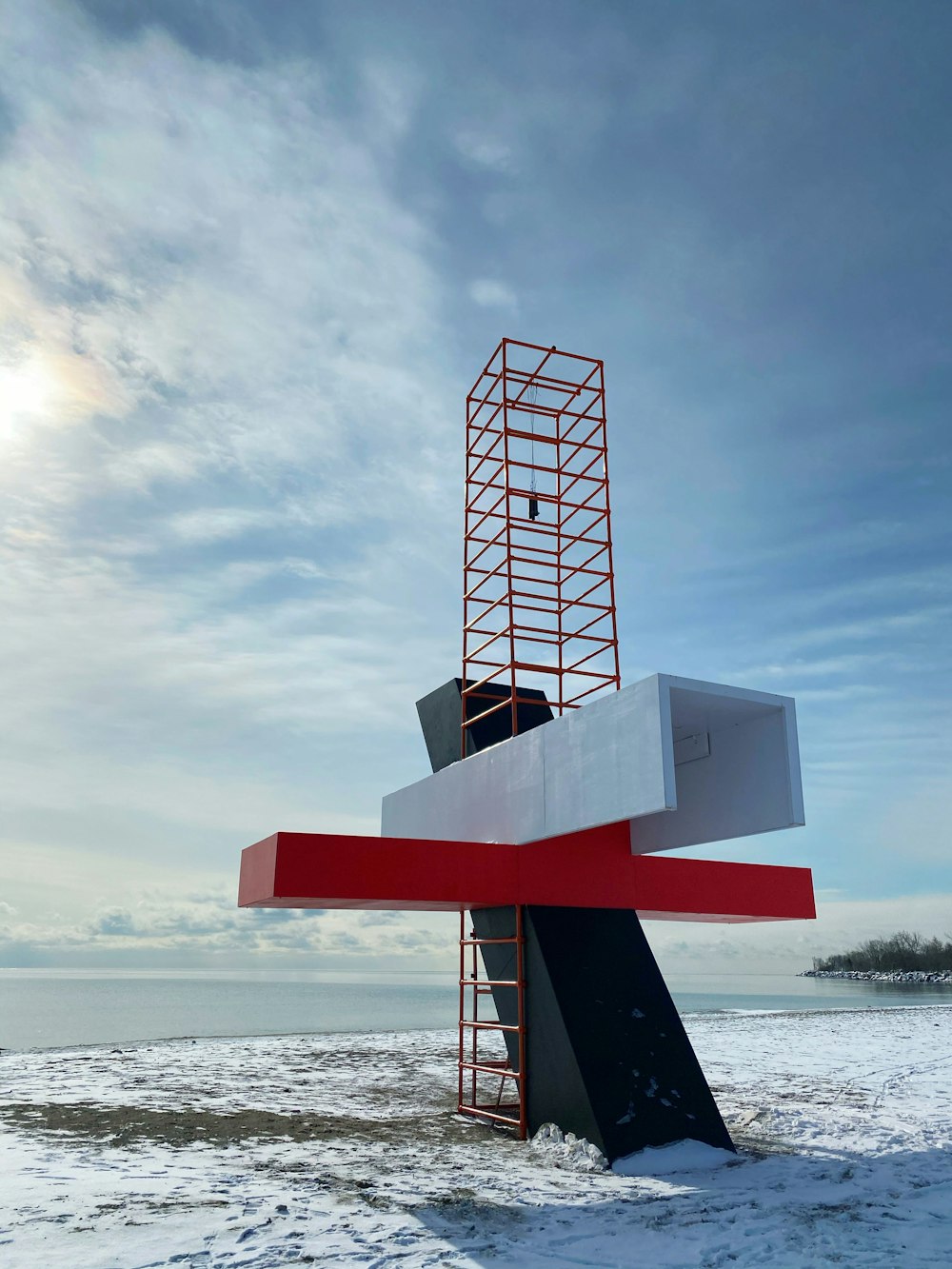 red and white metal tower near sea under white clouds