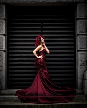 woman in red dress standing near brown brick wall