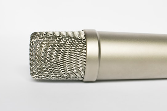 A close-up of a silver microphone with a metal mesh grille, captured on a plain white background. The design is sleek and cylindrical, showcasing intricate details of the grille and offering a modern and professional aesthetic.