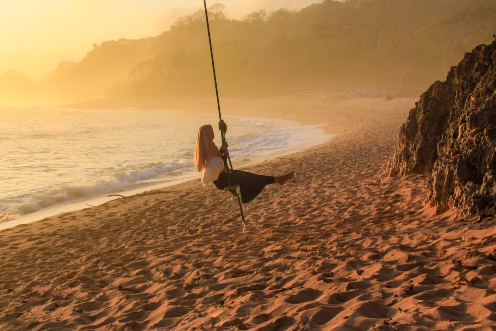 femme en robe blanche assise sur balançoire sur la plage pendant la journée