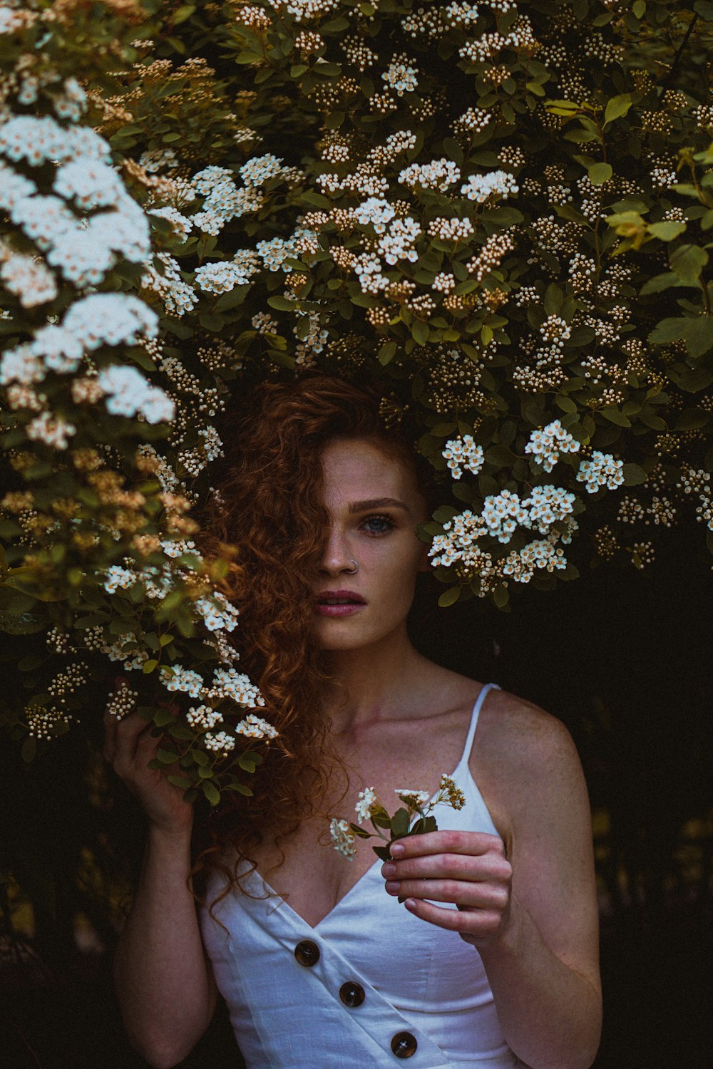 woman in white tank top standing under white flowers