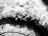 A close-up view of a textured surface, possibly fabric or carpet, with intricate details of fibers and threads visible. The black and white image highlights the contrast and patterns formed by the tightly woven material.