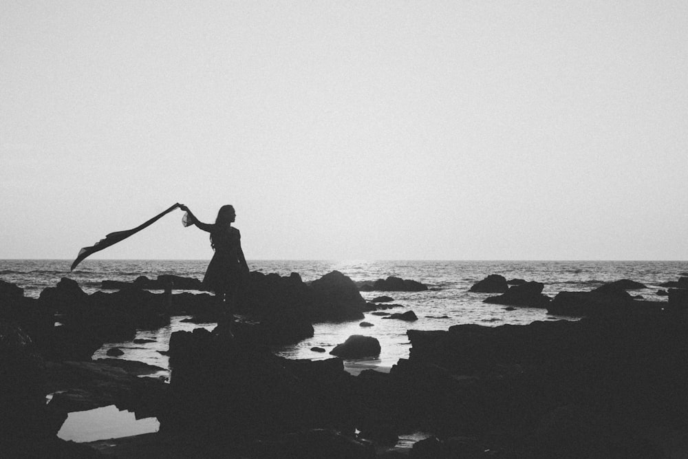 silhouette of person sitting on rock near body of water during daytime