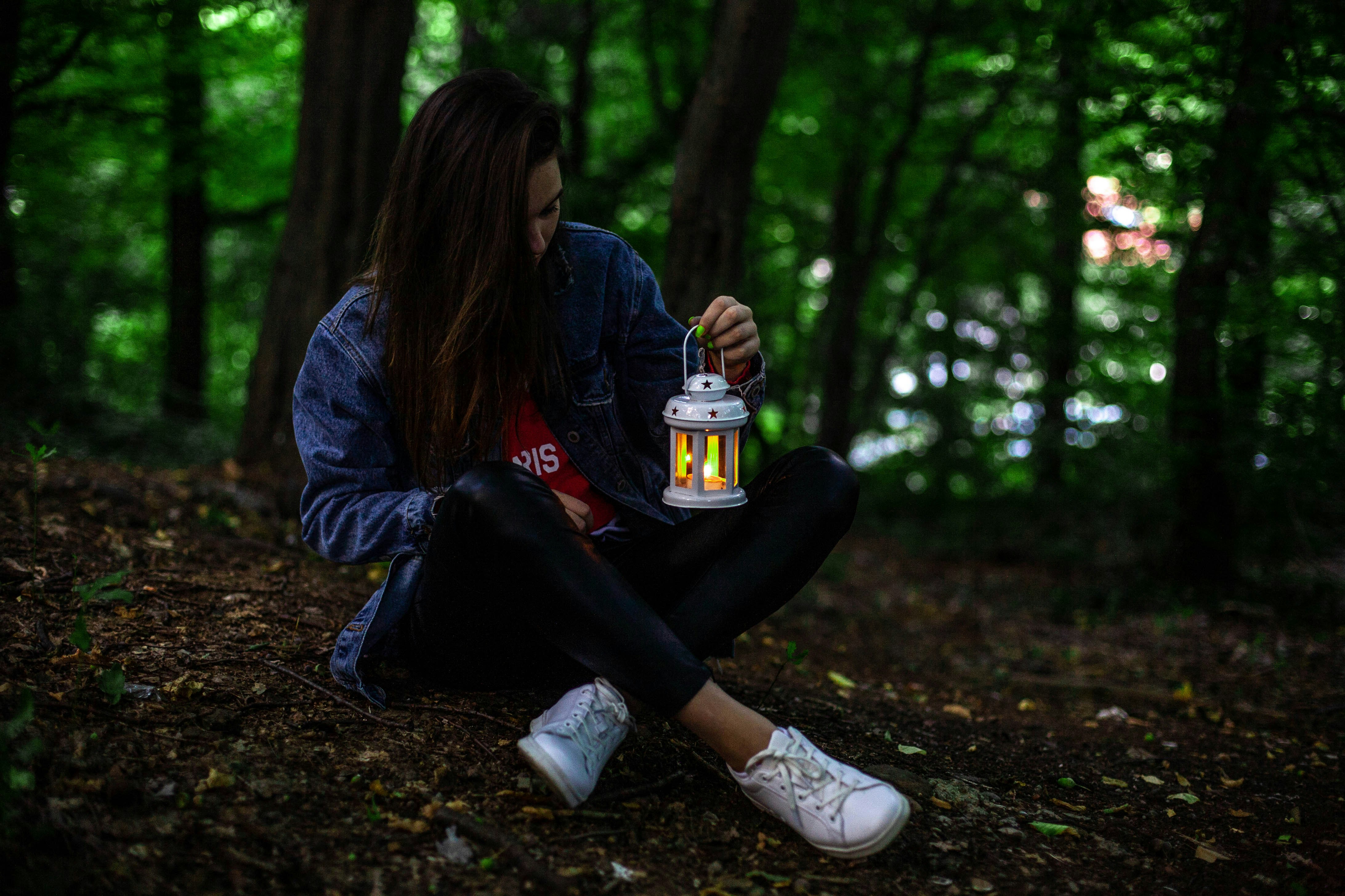 woman in blue jacket and black pants sitting on ground with dried leaves