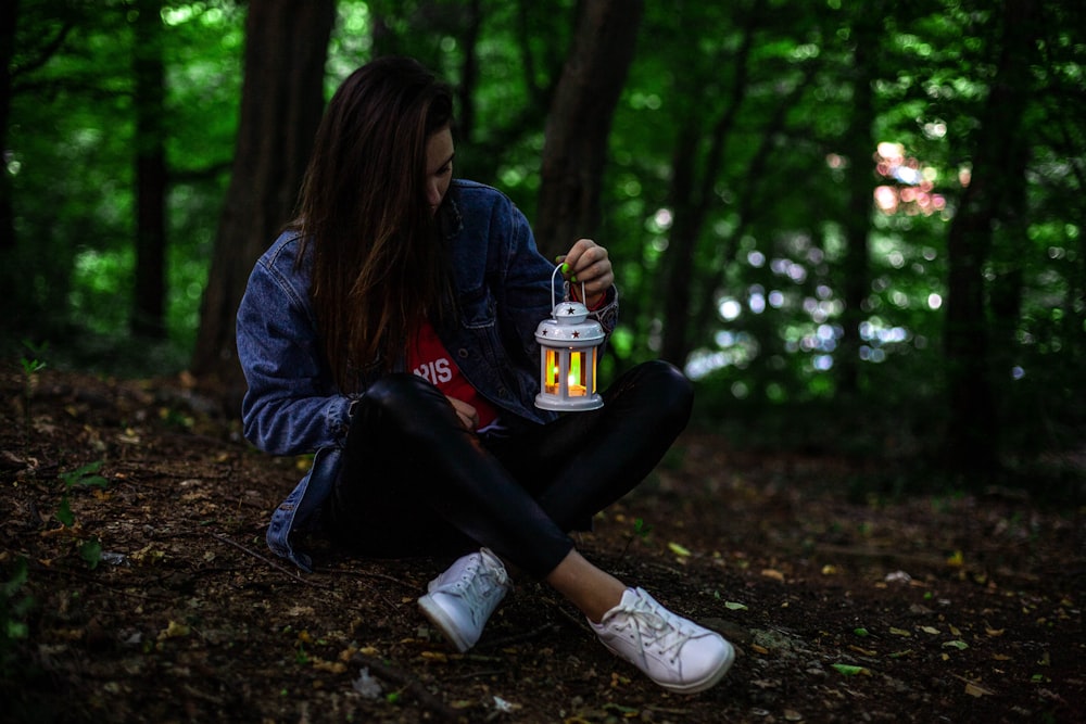 woman in blue jacket and black pants sitting on ground with dried leaves