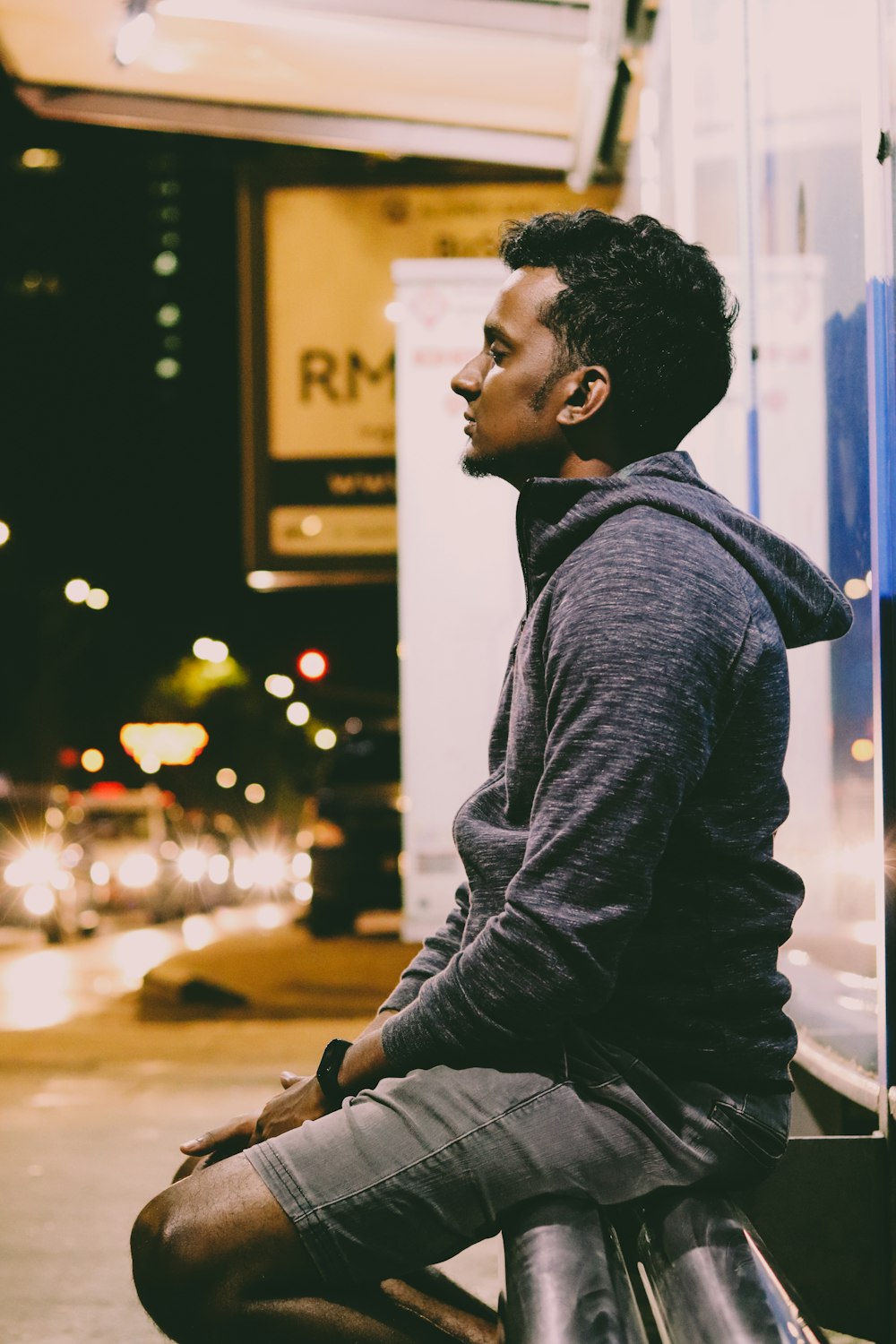 man in black leather jacket sitting on the sidewalk during night time