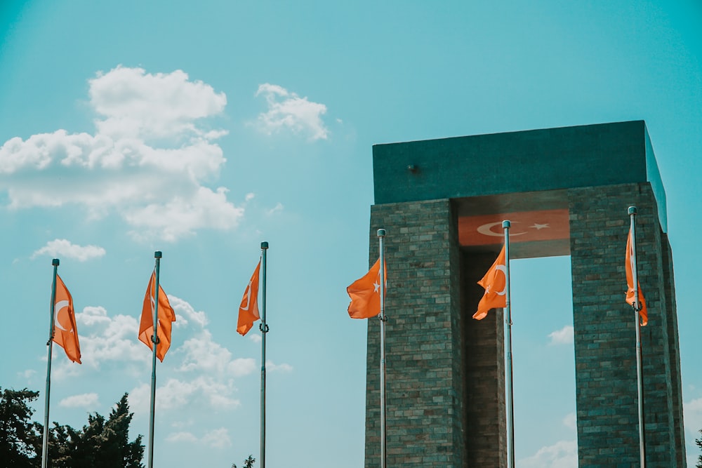 three flags on gray concrete wall under white clouds and blue sky during daytime