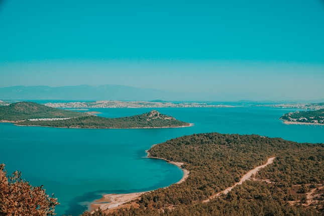 A serene coastal landscape featuring turquoise waters surrounded by lush green islands. The horizon shows a distant view of hills under a clear blue sky.