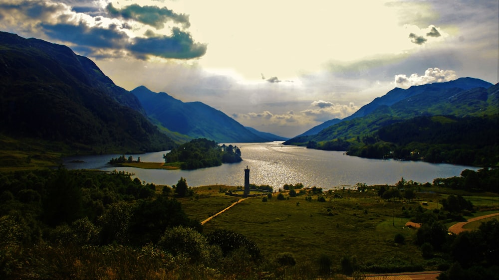 green mountains near body of water under white clouds during daytime