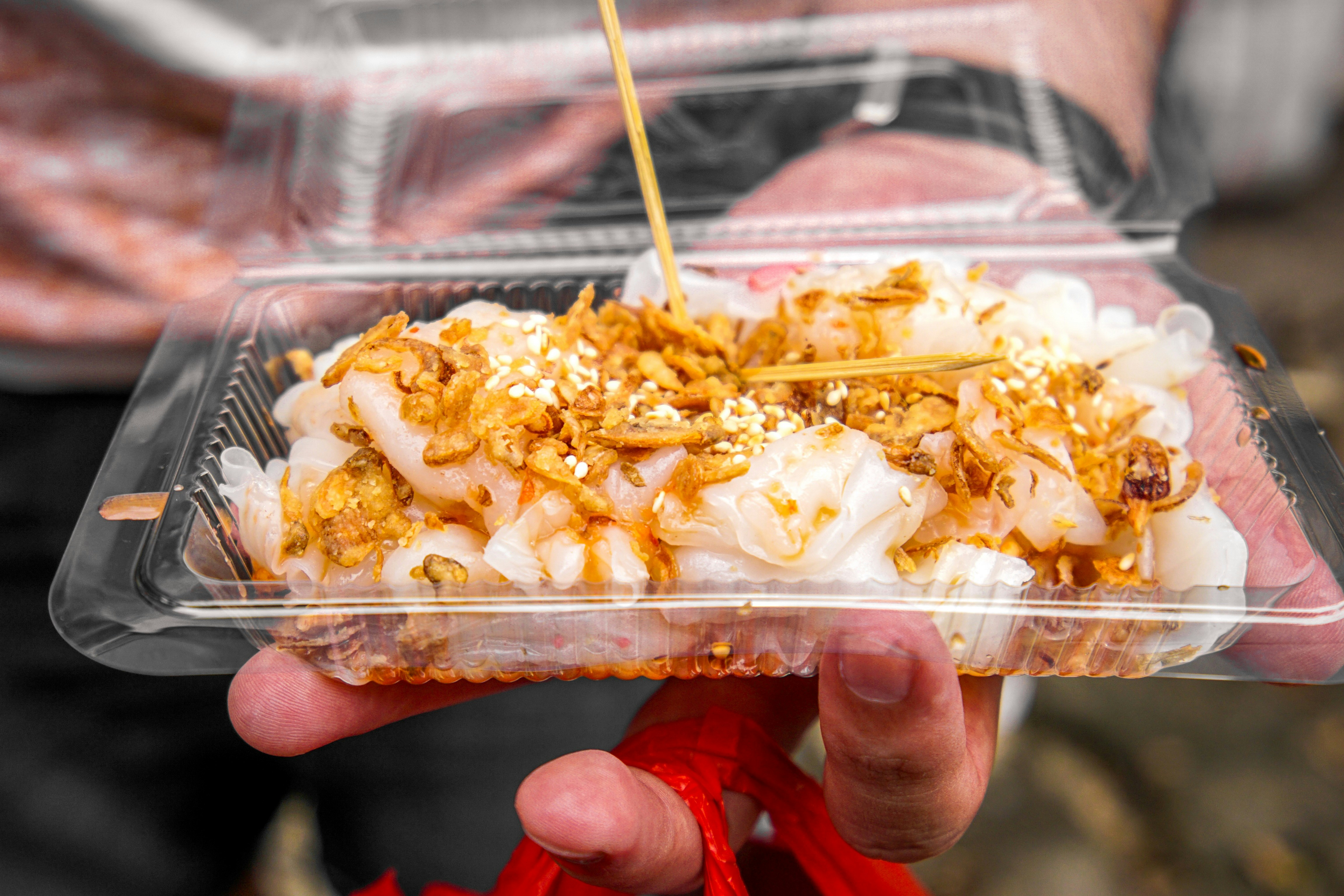 Hand holding a clear takeaway container of rice noodles