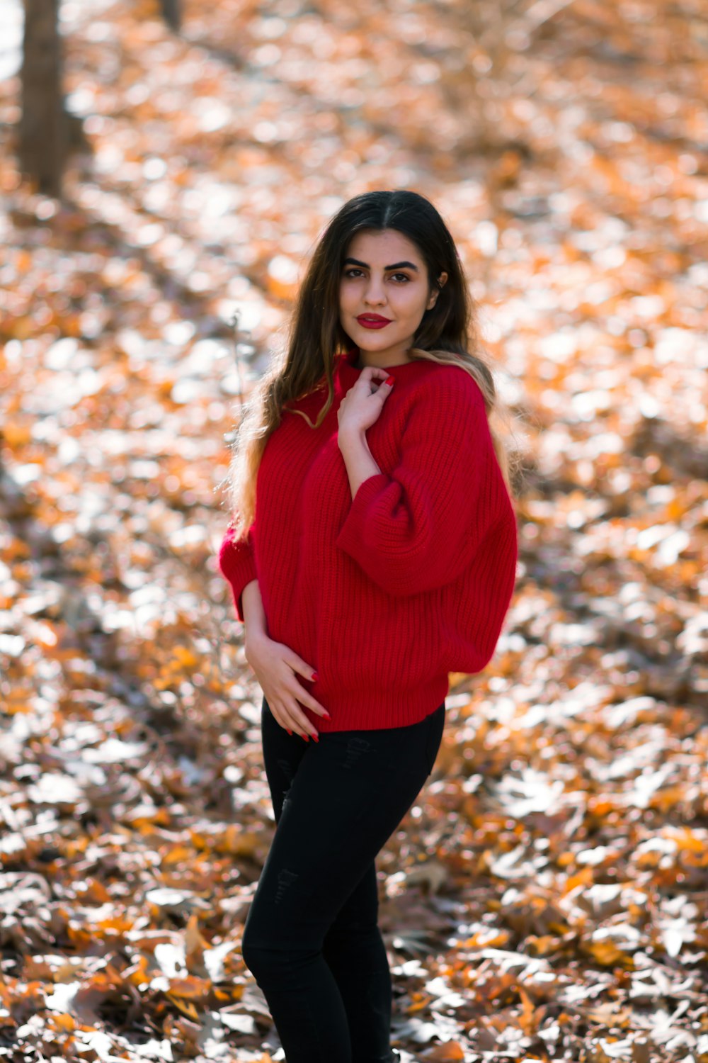 woman in red sweater and black pants standing on brown leaves during daytime