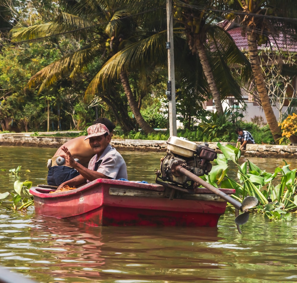 2 men riding red boat on river during daytime