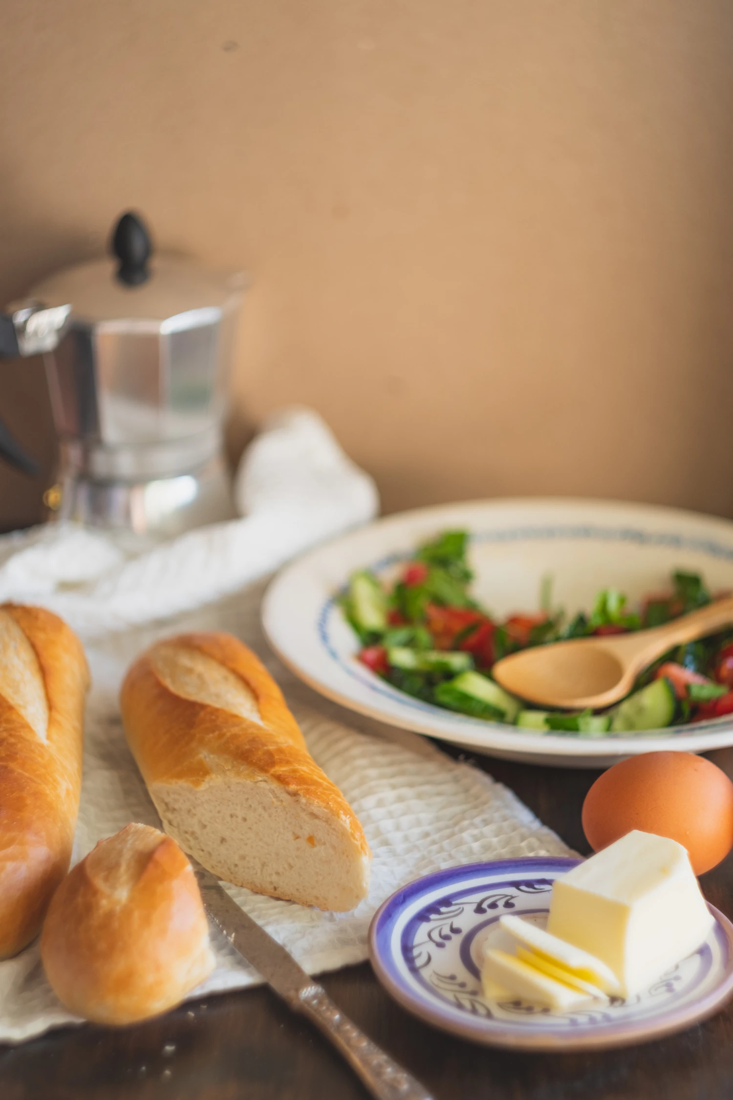 Bread, a moka pot and a plate of tomatoes laid out on a cloth