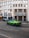 A vibrant green sports car is parked on a street in front of a building with large windows and signage that reads 'Credito Bergamasco'. The building has a modern architectural style with a series of vertical lines and is situated in an urban environment with tram tracks visible on the road. A few other cars are parked nearby, and pedestrians can be seen in the background.